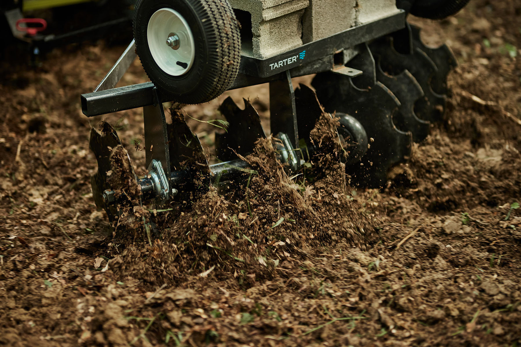 A tractor-mounted disc harrow cuts through dark soil in a close-up equipment photograph.