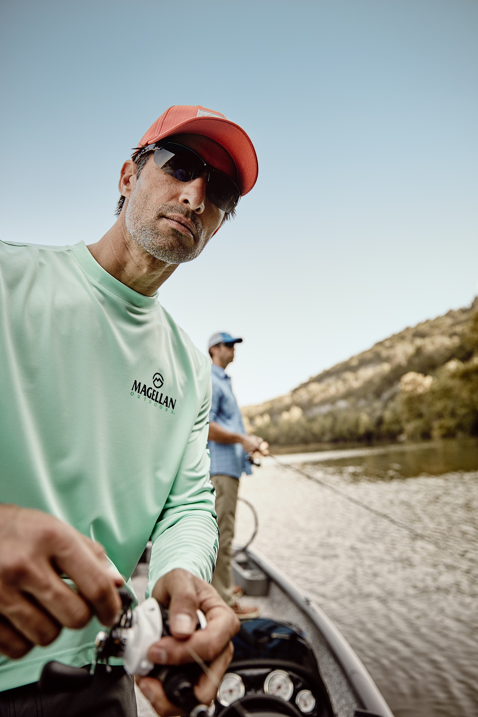 A man in a red cap and pale green shirt handles a fishing reel from a small boat.