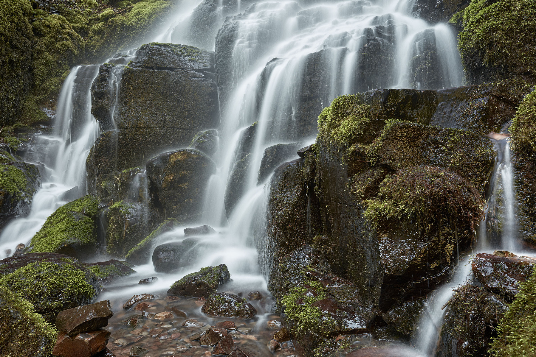 Water cascades over moss-covered rocks in a layered waterfall.