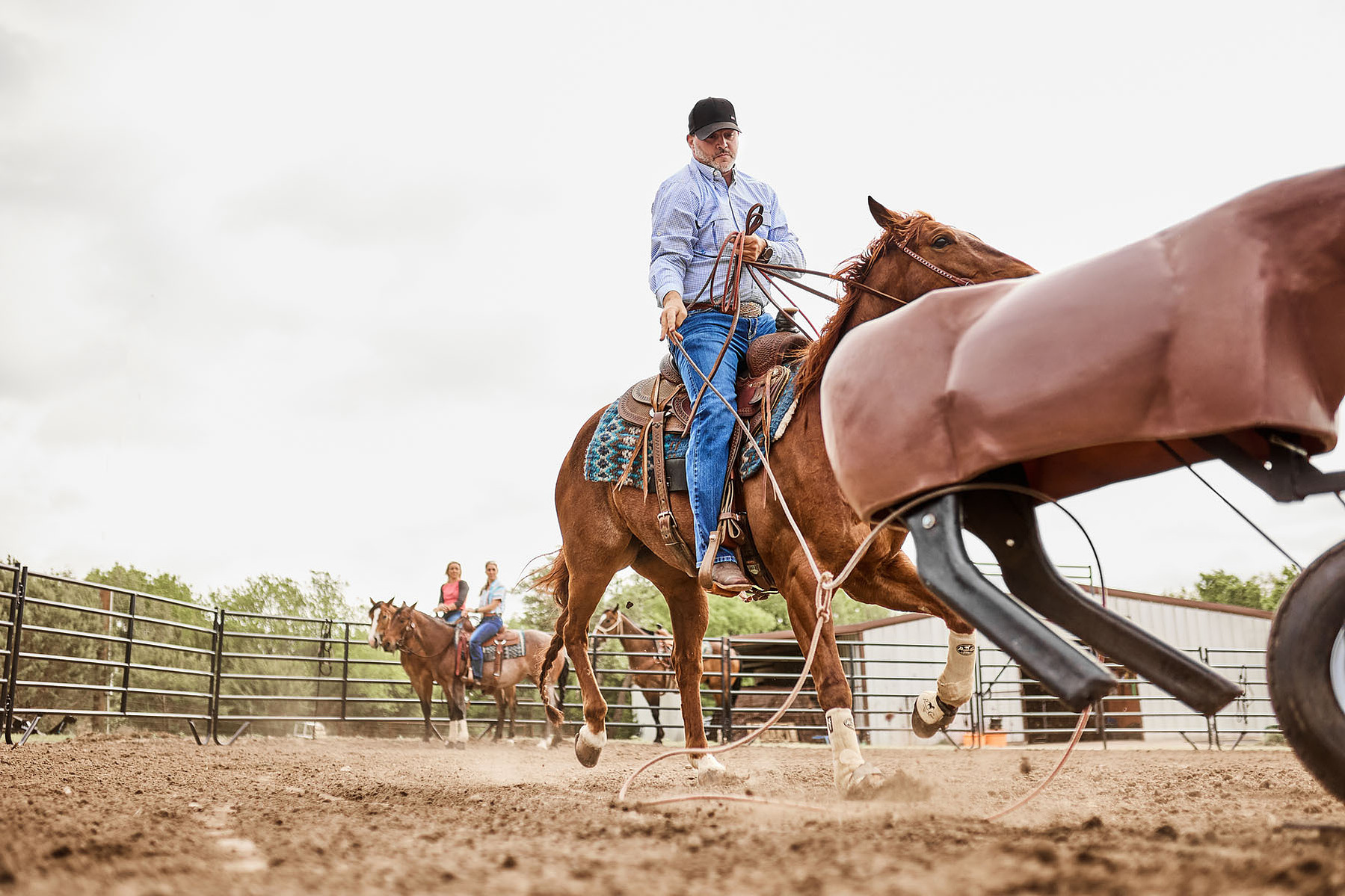 A rider on a chestnut horse waits in a dirt arena, photographed beside another saddle.