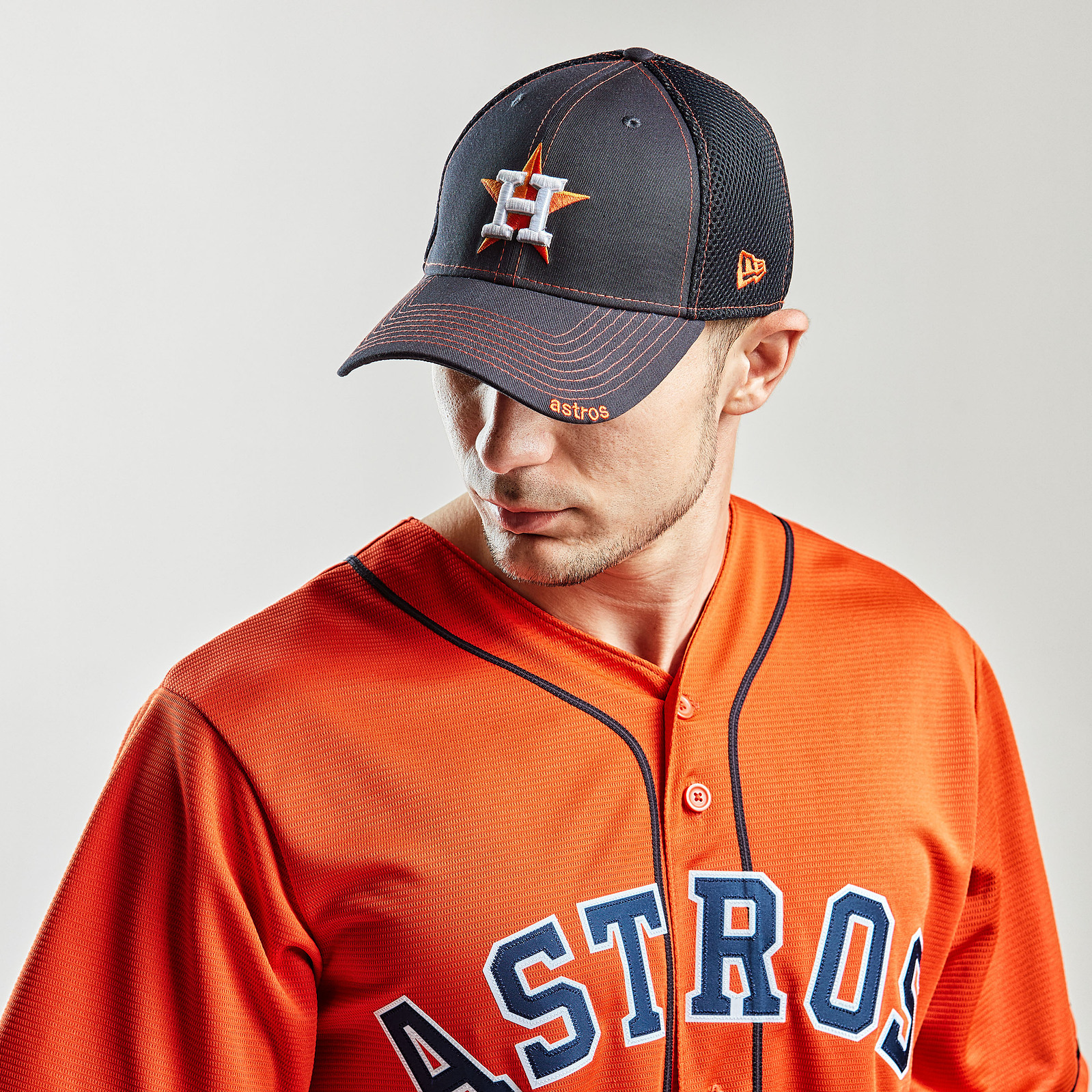 A man wears an orange Astros baseball jersey and dark cap against a pale studio background.
