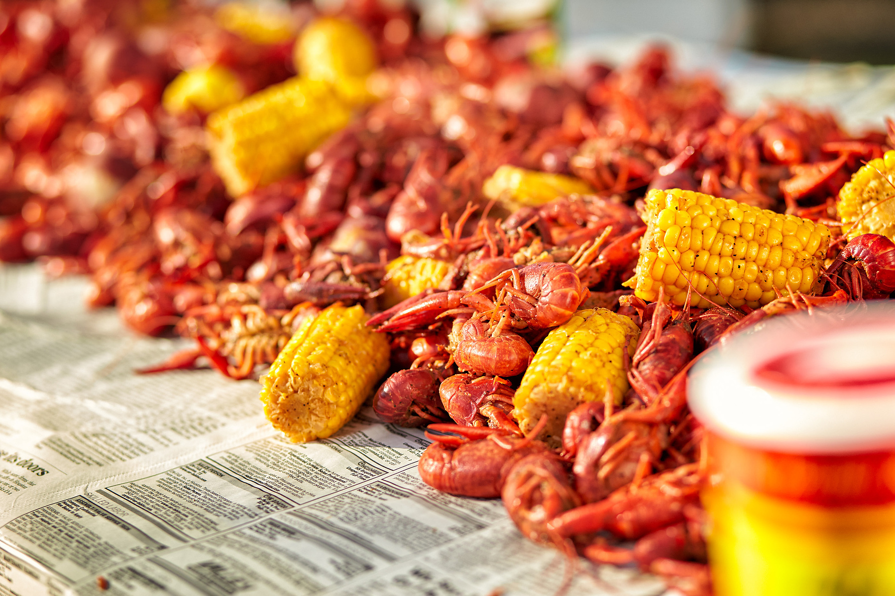 Cooked crawfish and pieces of corn spread across newspaper in warm light.