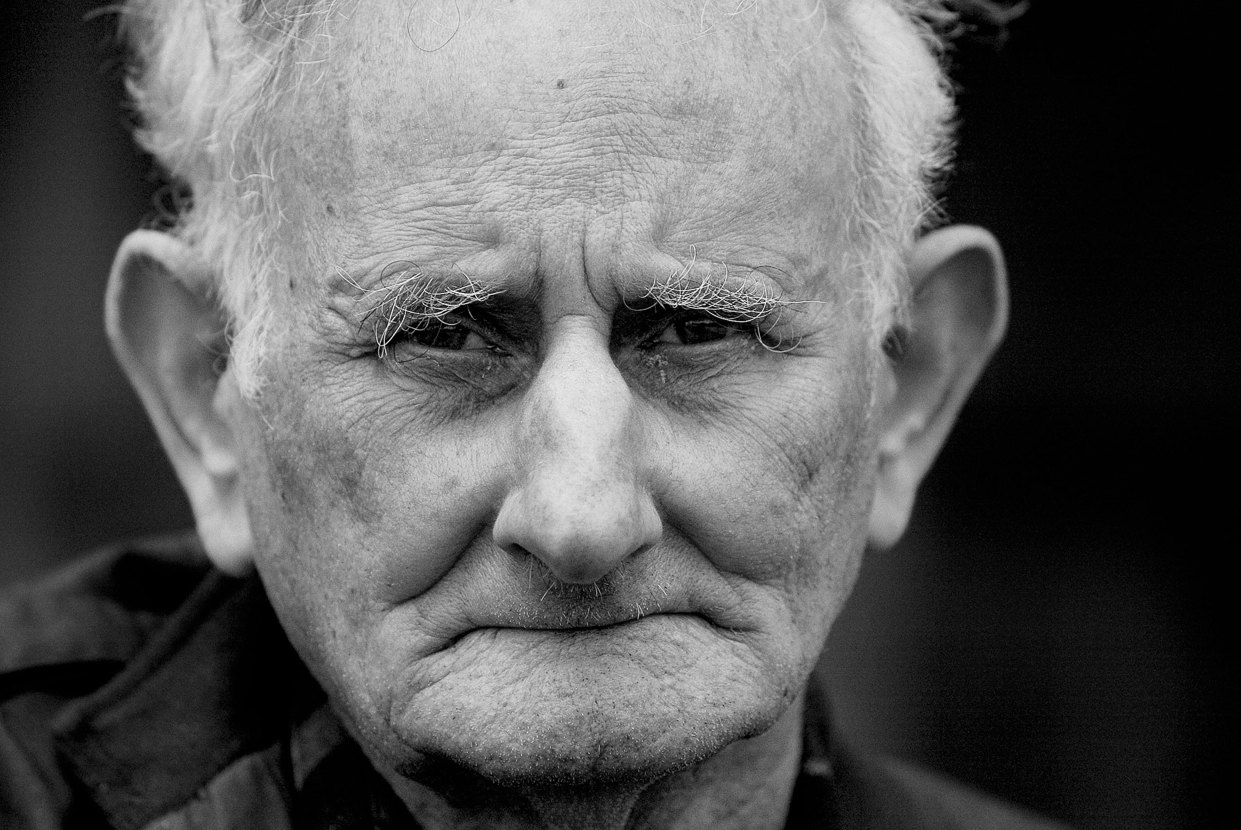 A black-and-white close-up portrait of an older man looking directly toward the camera.