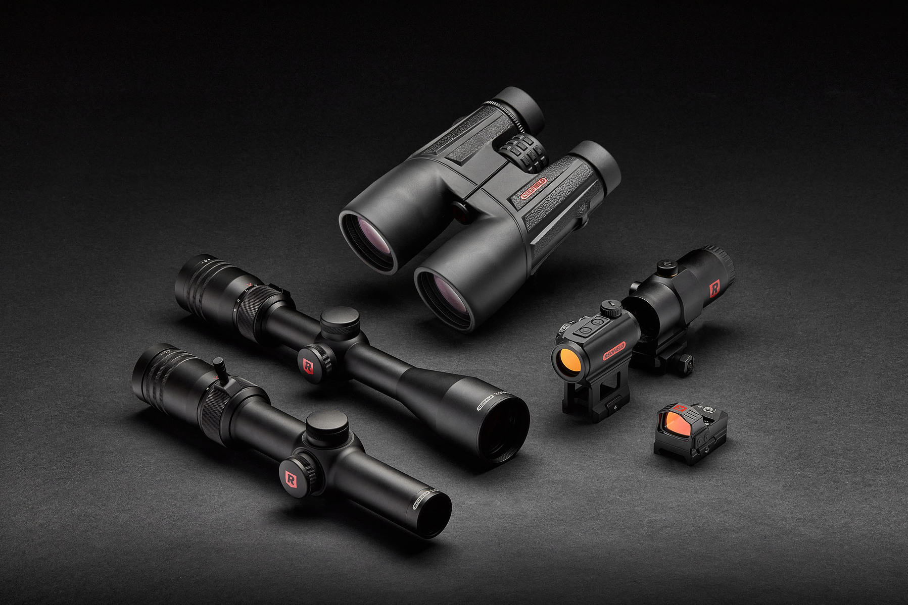 Binoculars, riflescopes, and compact optical sights arranged against a black studio background.