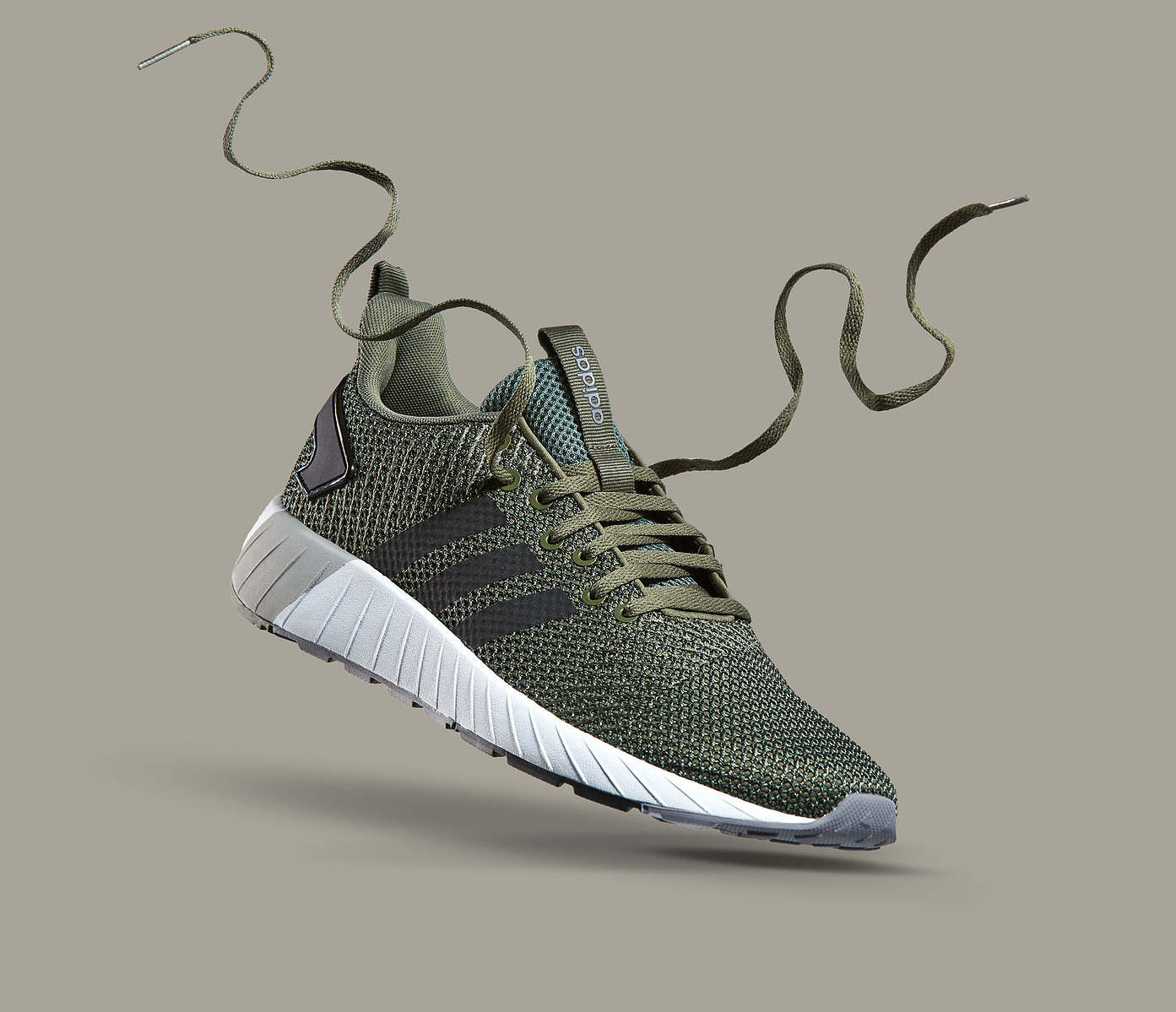 A green knit athletic shoe appears suspended with its laces curling above it.