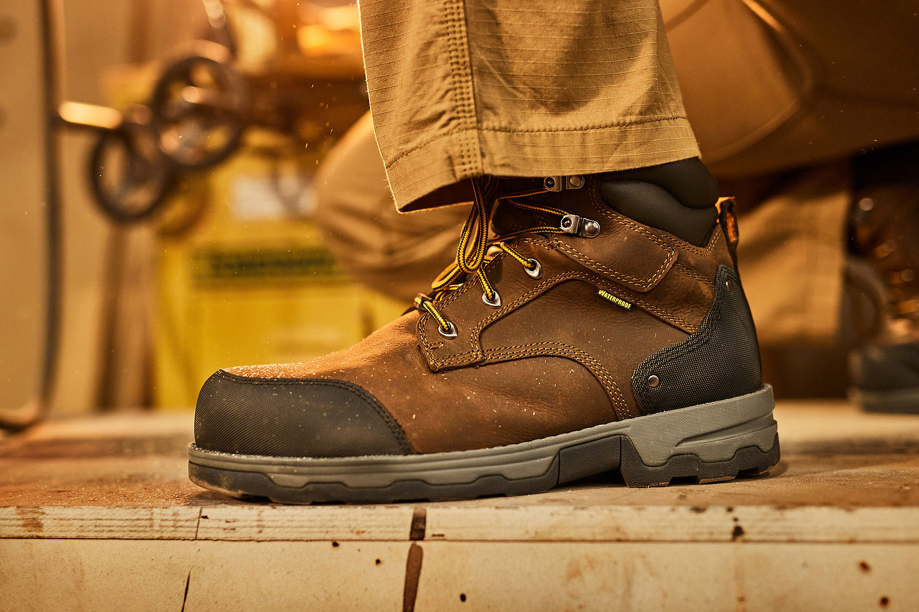 Close-up of a brown work boot worn on a wooden step in warm workshop light.