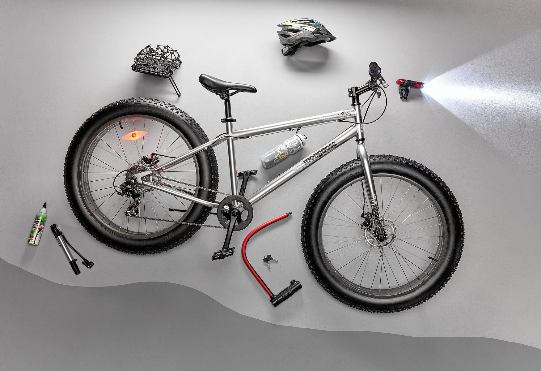 A bicycle, helmet, tools, water bottle, and accessories arranged overhead on gray.
