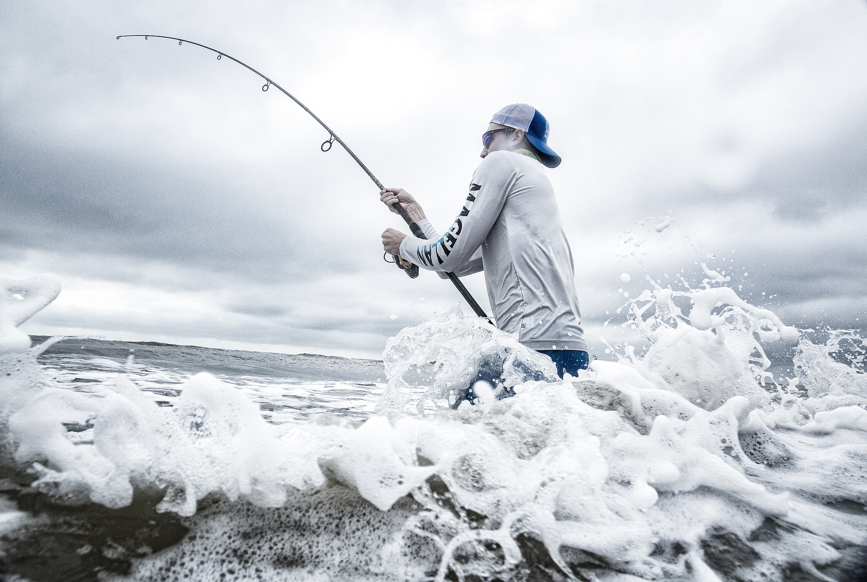 An angler holds a bent fishing rod while waves break around them.