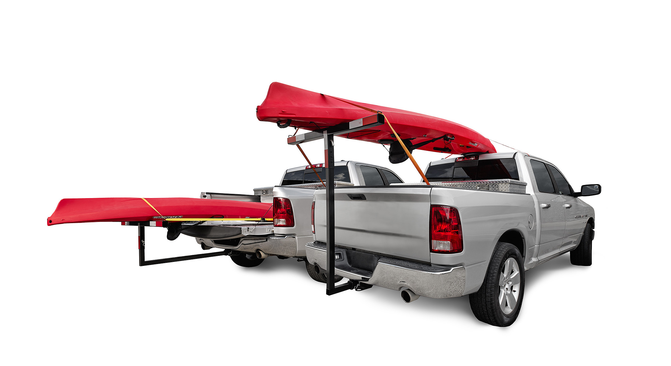 A silver pickup truck carries two red kayaks on an extended rack against a white background.