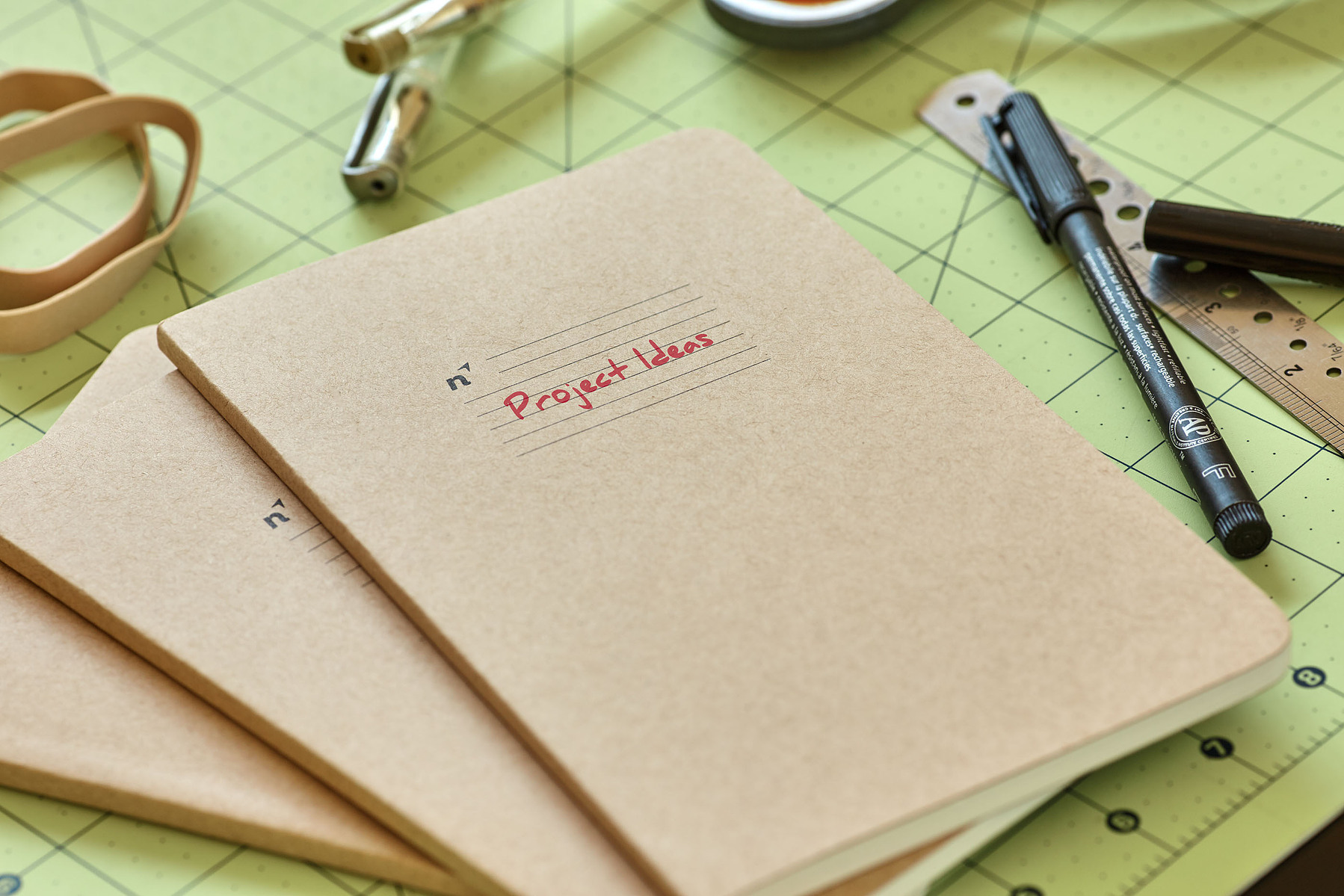 A kraft-paper notebook labeled Project Ideas sits with drafting tools on a gridded cutting mat.