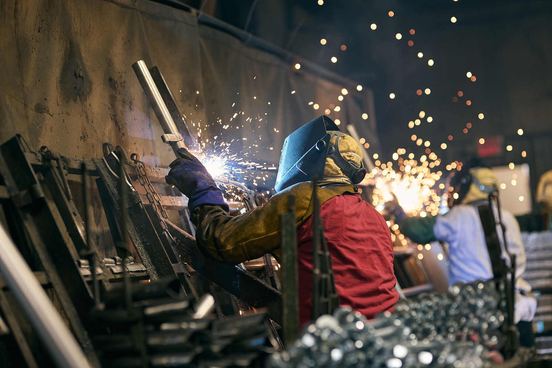 A welder in protective clothing joins a metal structure amid bright sparks.