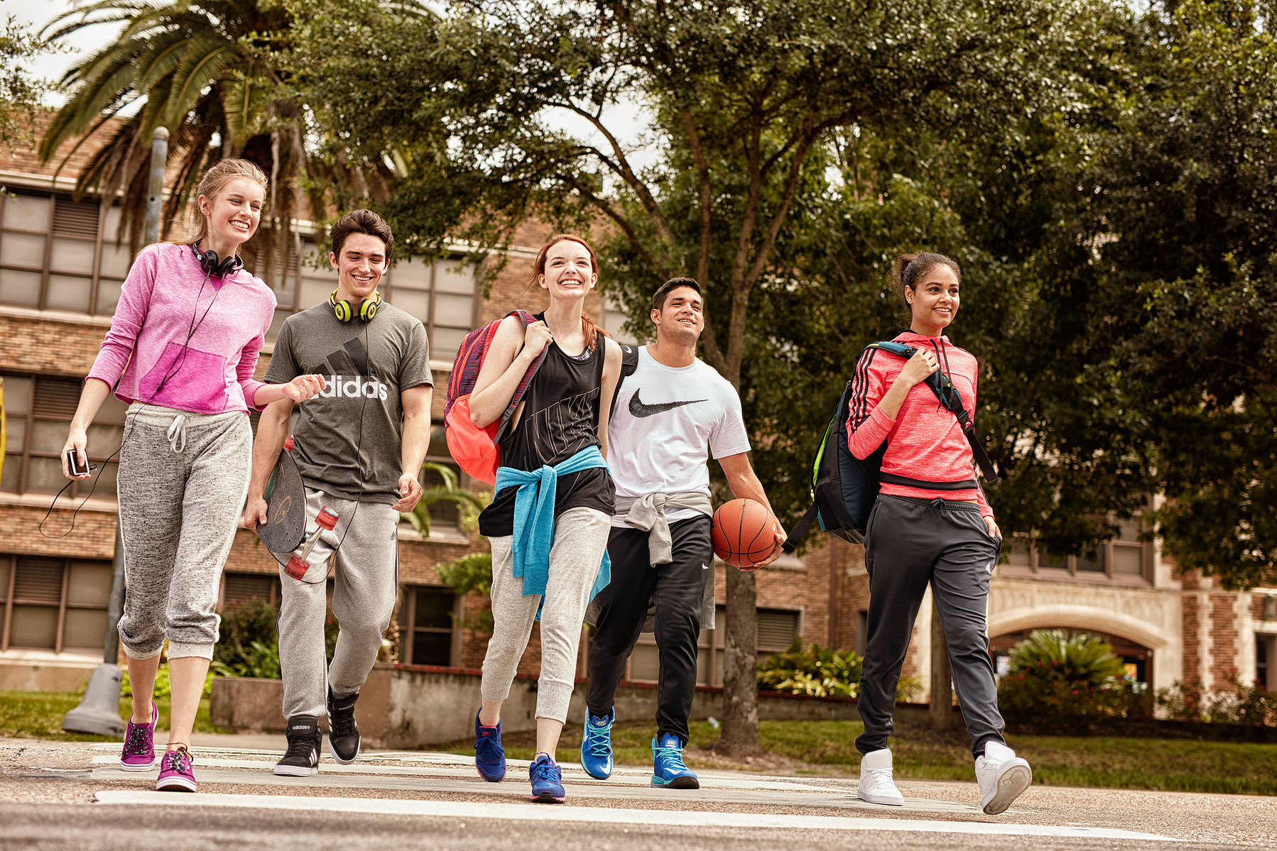 Five people in athletic clothing walk outdoors carrying sports gear and a basketball.