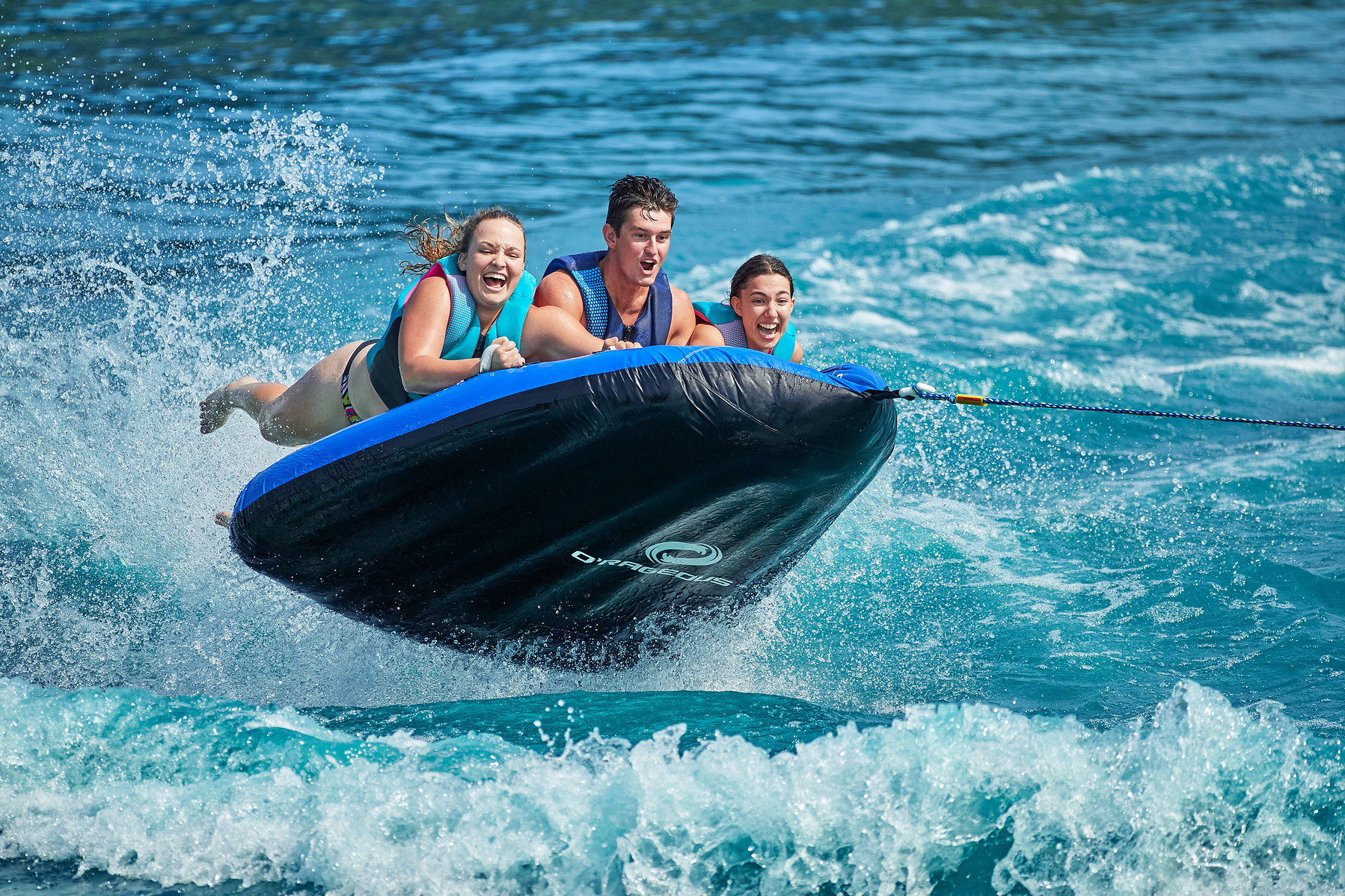 Three people ride an inflatable towable over choppy blue water.